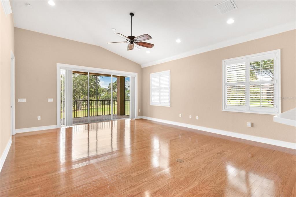 An empty living room features hardwood floors, a vaulted ceiling with a fan, and sliding doors — 14 CAMINO REAL BOULEVARD UNIT 14, HOWEY IN THE HILLS, FL