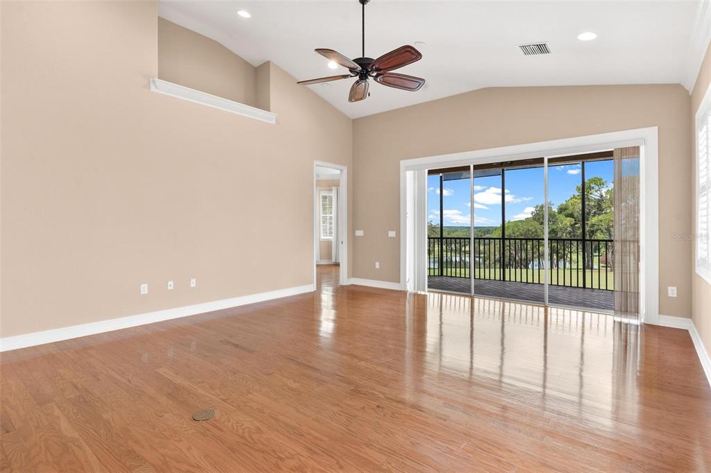 A spacious living room with hardwood floors, a vaulted ceiling, and sliding glass doors to a balcony — 14 CAMINO REAL BOULEVARD UNIT 14, HOWEY IN THE HILLS, FL