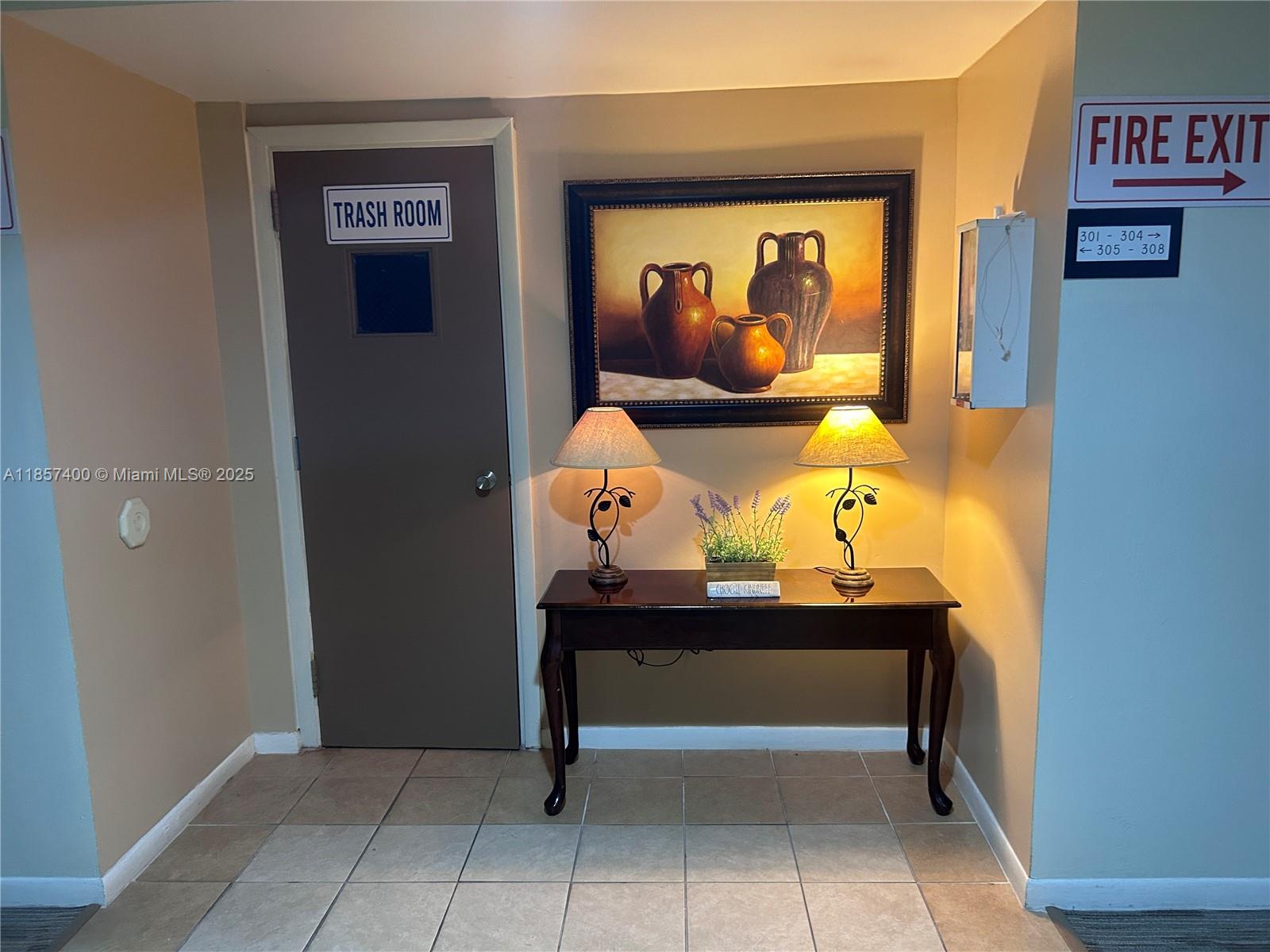 A hallway features a trash room door, a console table with lamps, and wall art — 14201 SW 66th St # 306, Miami FL 33183, MIAMI, FL