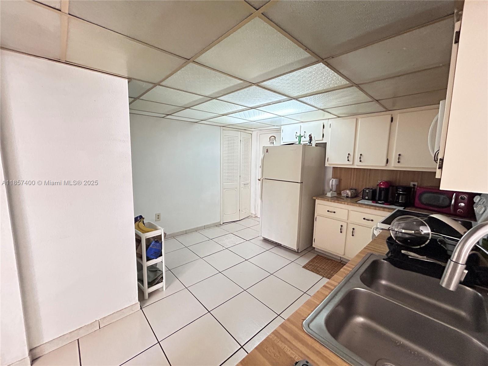 A kitchen features white cabinets, a drop ceiling, tile flooring, and a double-basin sink — 14201 SW 66th St # 306, Miami FL 33183, MIAMI, FL