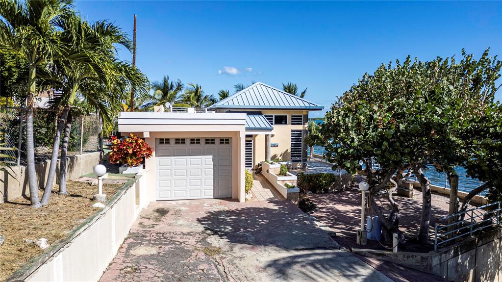A single-story house with a white garage and a metal roof sits near the water — 11 CALLE A, GUANICA, PR