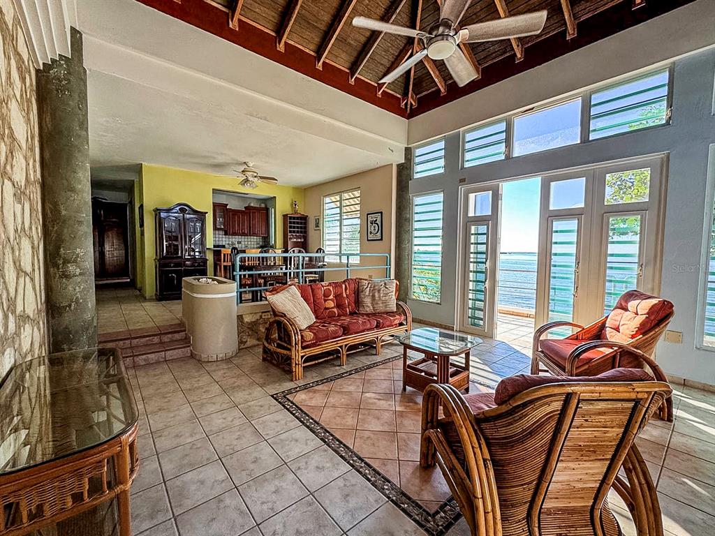 A living room with rattan furniture, tile floors, and a vaulted ceiling overlooking the ocean — 11 CALLE A, GUANICA, PR