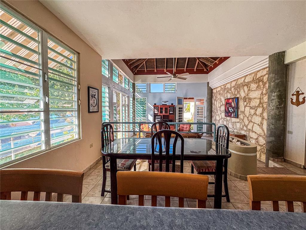 A dining area with a glass table, wooden chairs, stone wall, and large windows — 11 CALLE A, GUANICA, PR