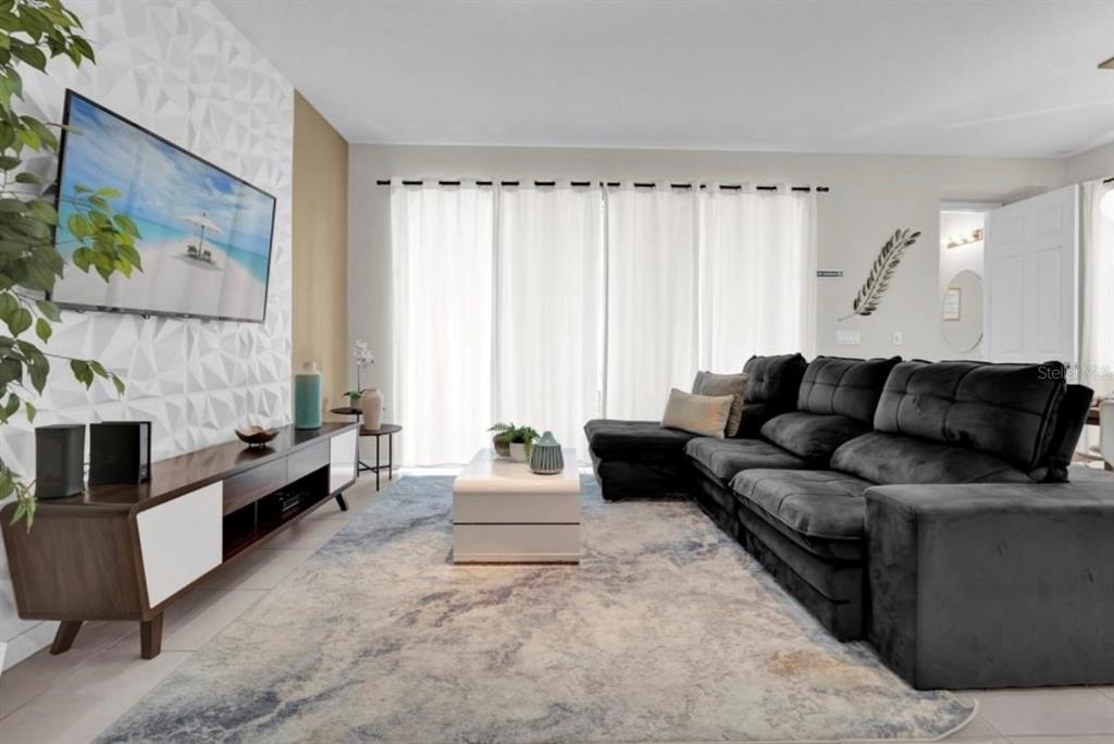 A living room features a dark sectional sofa, a patterned area rug, and a wall-mounted television — 1549 CAREY PALM CIRCLE, KISSIMMEE, FL