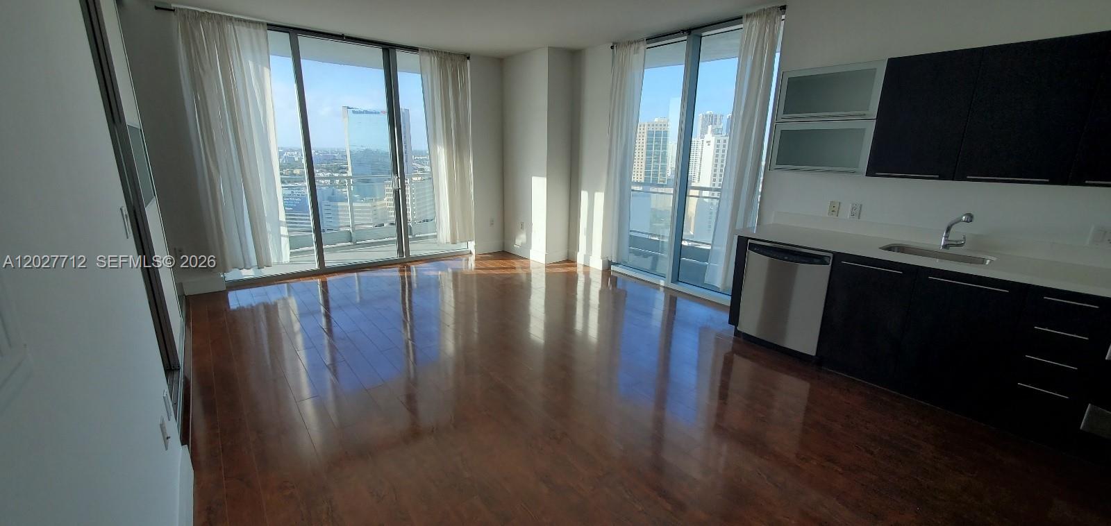 A modern kitchen with dark cabinets and stainless appliances opens into a sunlit living area — 90 SW 3rd St # 2705, Miami FL 33130, MIAMI, FL