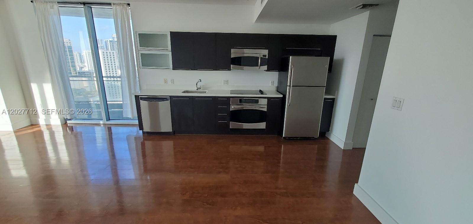 A modern kitchen features dark cabinetry, stainless steel appliances, and light countertops with city views — 90 SW 3rd St # 2705, Miami FL 33130, MIAMI, FL