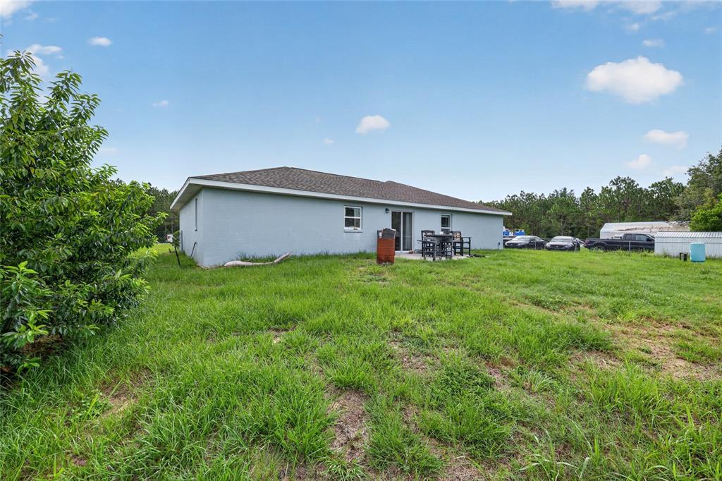 The exterior of a single-story house with a backyard, patio, and surrounding grassy area — 8 ALMOND DRIVE TRACE, OCALA, FL