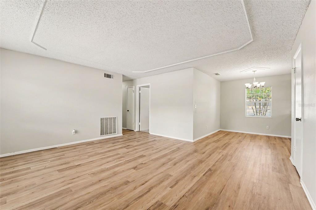 An empty room with light wood-look flooring, a textured ceiling, and a dining area window — 8308 OLEANDER LANE, TAMPA, FL