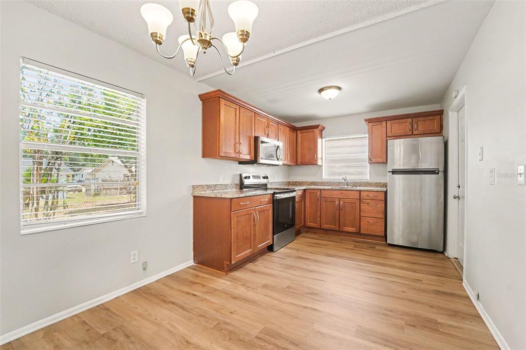 A kitchen with wood cabinets, stainless steel appliances, granite countertops, and light wood-look flooring — 8308 OLEANDER LANE, TAMPA, FL
