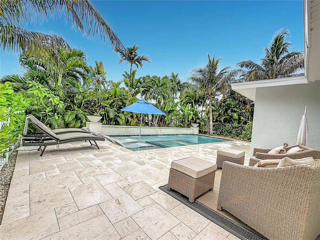 A patio with stone pavers, lounge chairs, and wicker furniture overlooks a swimming pool — 2931 ALTON DRIVE, ST PETE BEACH, FL