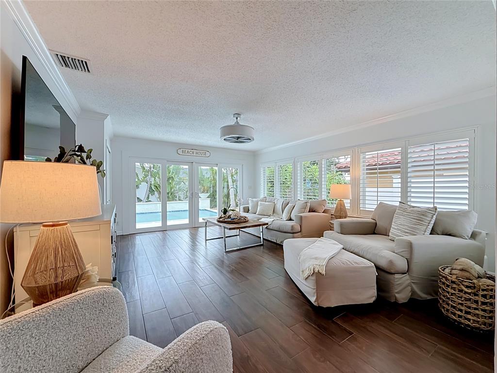A living room features dark wood-look tile floors, neutral furniture, and sliding glass doors to a pool — 2931 ALTON DRIVE, ST PETE BEACH, FL