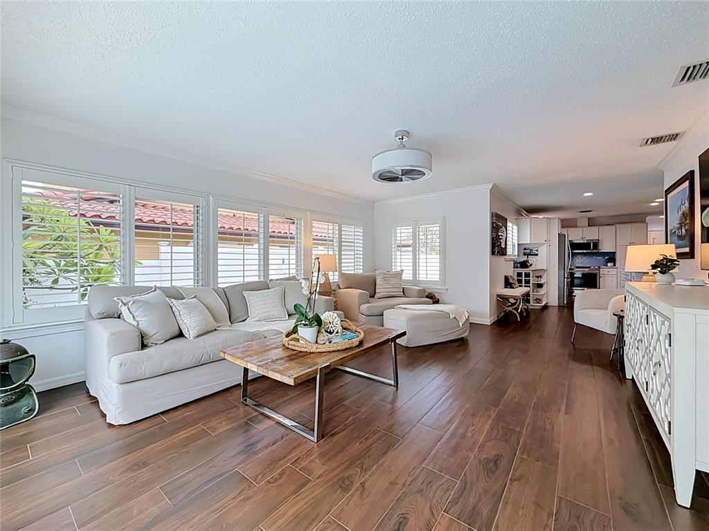 A living room with wood-look tile floors, a beige sofa, and a view of a tiled roof — 2931 ALTON DRIVE, ST PETE BEACH, FL