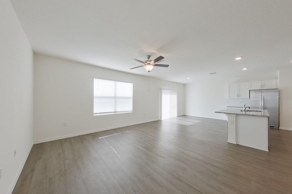 An open-concept living area features light wood-look flooring, a ceiling fan, and a kitchen island — 32048 KATELIN CIRCLE, LEESBURG, FL