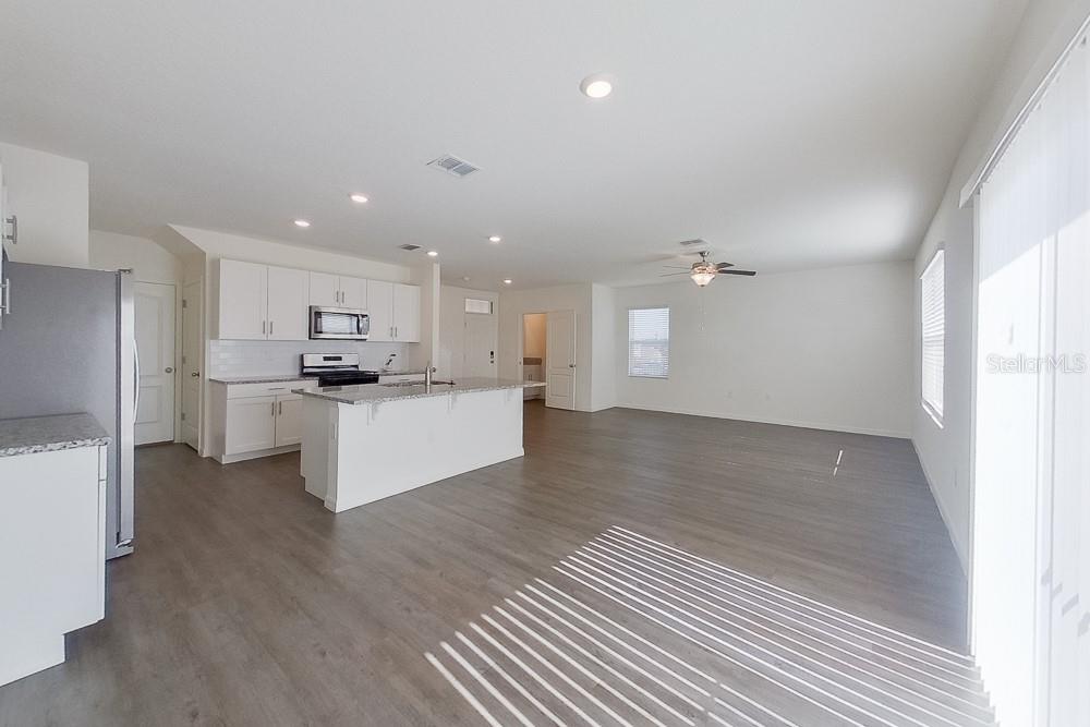 An open-concept kitchen and living area with white cabinets, granite countertops, and wood-look flooring — 32048 KATELIN CIRCLE, LEESBURG, FL