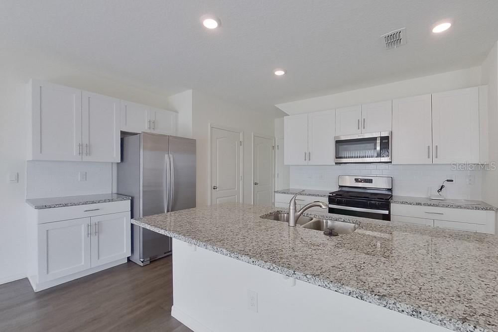 A kitchen features white cabinets, granite countertops, stainless steel appliances, and a central island — 32048 KATELIN CIRCLE, LEESBURG, FL