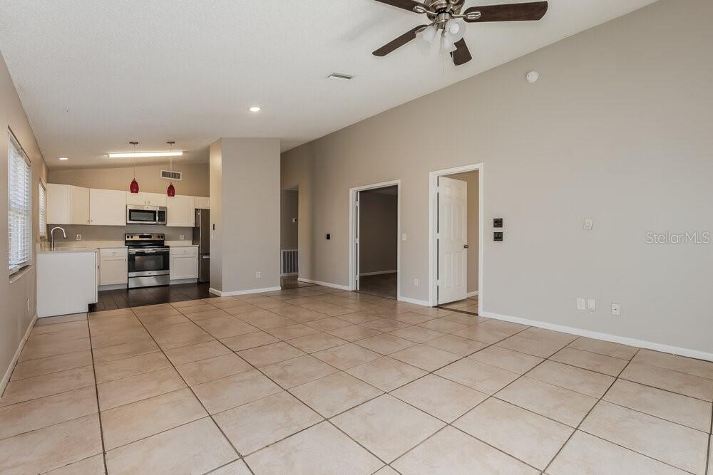 A spacious room with light tile flooring, a vaulted ceiling, and an open-concept kitchen — 2027 HELM LANE, VALRICO, FL
