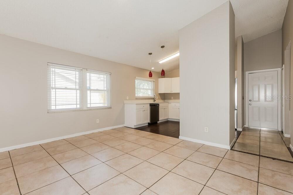 An open-concept kitchen and dining area features white cabinets, tile flooring, and a front door — 2027 HELM LANE, VALRICO, FL