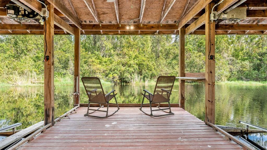 Two rocking chairs sit on a wooden boat dock overlooking a calm, tree-lined waterway — 237 KENT COURT, HAINES CITY, FL