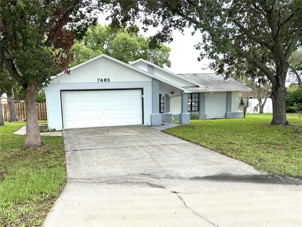 A single-story house with a white garage, light blue siding, and a concrete driveway — 7463 PHILATELIC DRIVE, SPRING HILL, FL