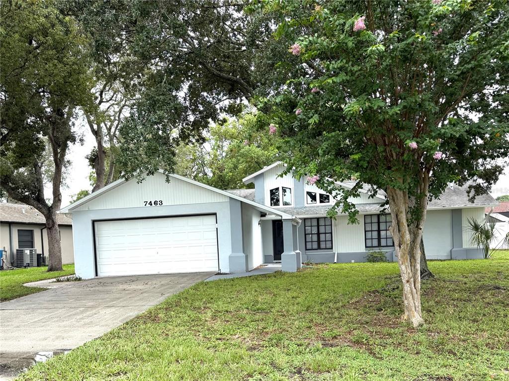 A light blue single-story house with a white garage door and a large flowering tree — 7463 PHILATELIC DRIVE, SPRING HILL, FL