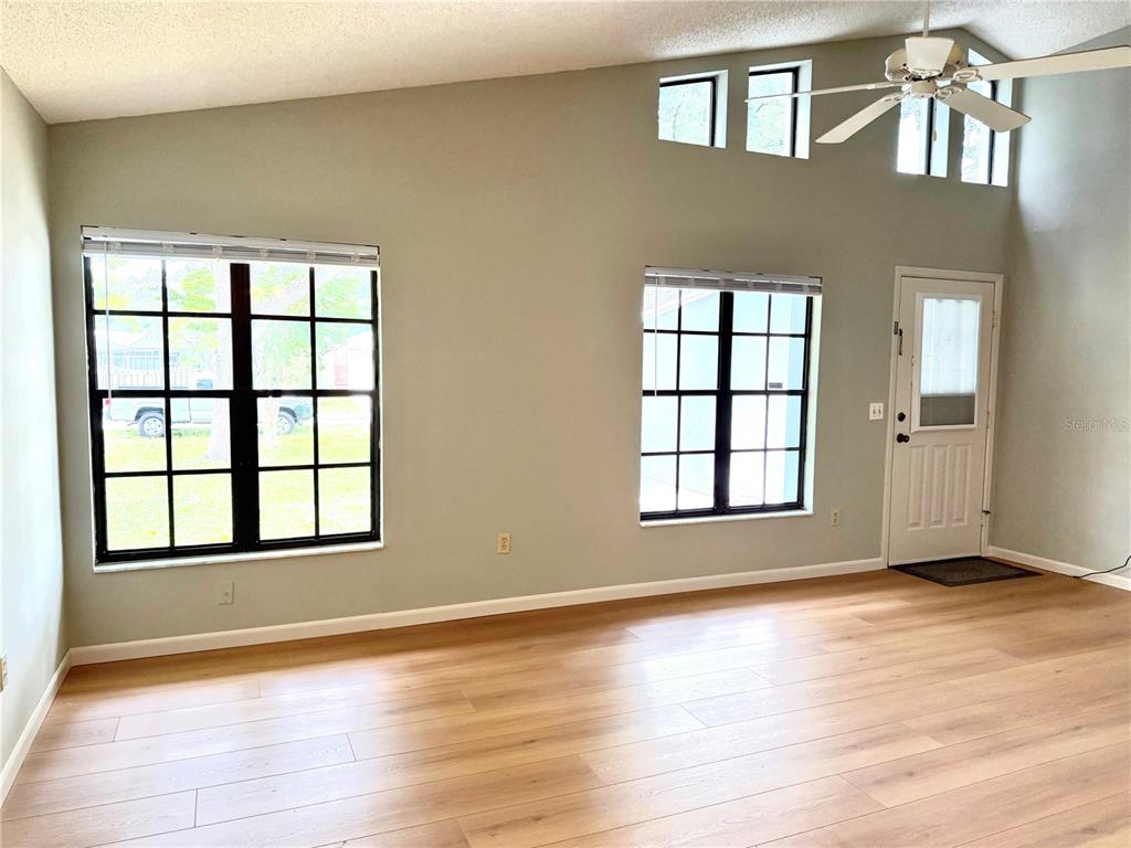 A living room features light wood-look flooring, two grid-pane windows, and a white entry door — 7463 PHILATELIC DRIVE, SPRING HILL, FL