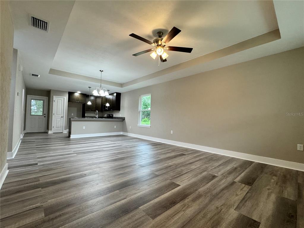 An open-concept living area features a tray ceiling, wood-look flooring, and an adjacent kitchen — 8523 SE 70TH AVENUE, TRENTON, FL
