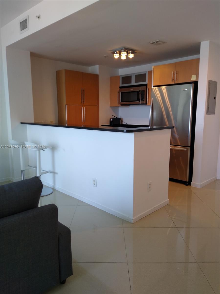 A kitchen features light wood cabinets, stainless steel appliances, and a black breakfast bar counter — 300 S Biscayne Blvd # 2905, Miami FL 33131, MIAMI, FL