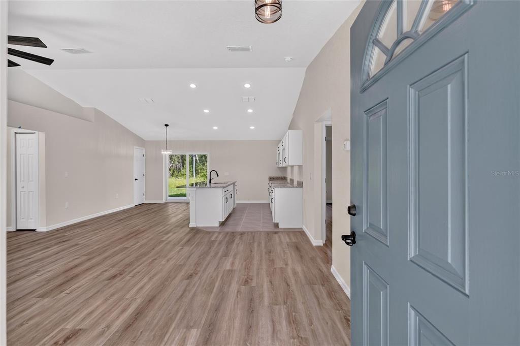 An open-concept living area features light wood flooring, white cabinetry, and a blue front door — 6 BAY PASS TERRACE, OCKLAWAHA, FL