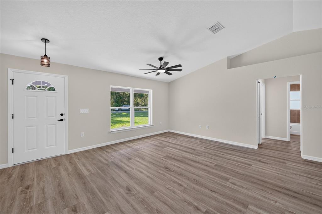 An empty living room features light-colored walls, wood-look flooring, a ceiling fan, and a front door — 6 BAY PASS TERRACE, OCKLAWAHA, FL