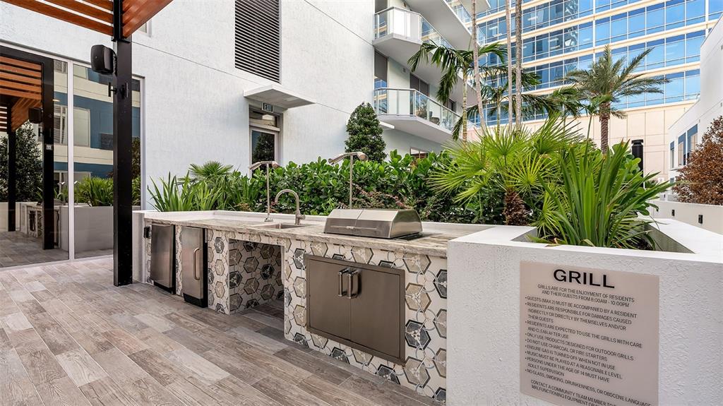 An outdoor kitchen area features a stainless steel grill, sink, and tiled counter on a patio — 225 1ST AVENUE N UNIT A2, ST PETERSBURG, FL