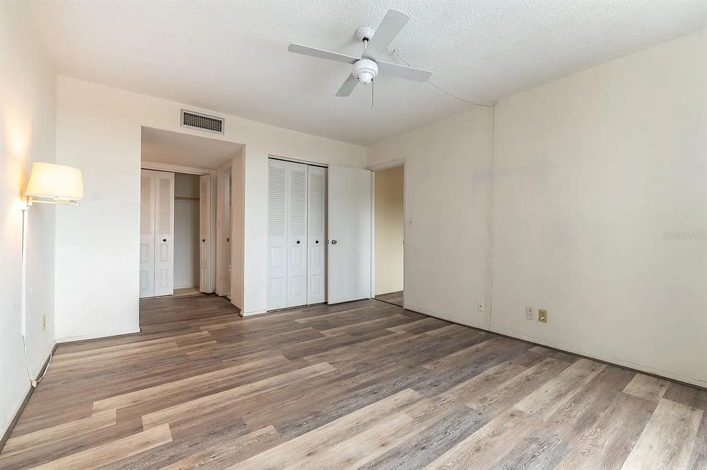A bedroom with light green walls, wood-look flooring, a ceiling fan, and two closets — 2901 26TH STREET W UNIT 309, BRADENTON, FL