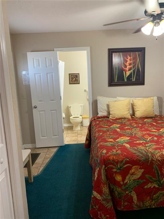 A bedroom features a bed with a tropical quilt, a ceiling fan, and an attached bathroom — 2777 N POINCIANA BOULEVARD UNIT 226G, KISSIMMEE, FL