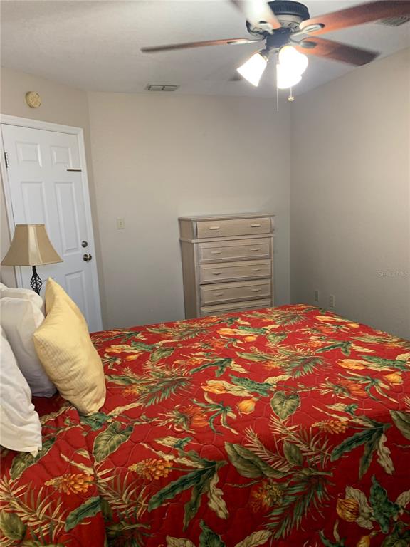 A bedroom features a bed with a tropical-print quilt, a dresser, and a ceiling fan — 2777 N POINCIANA BOULEVARD UNIT 226G, KISSIMMEE, FL