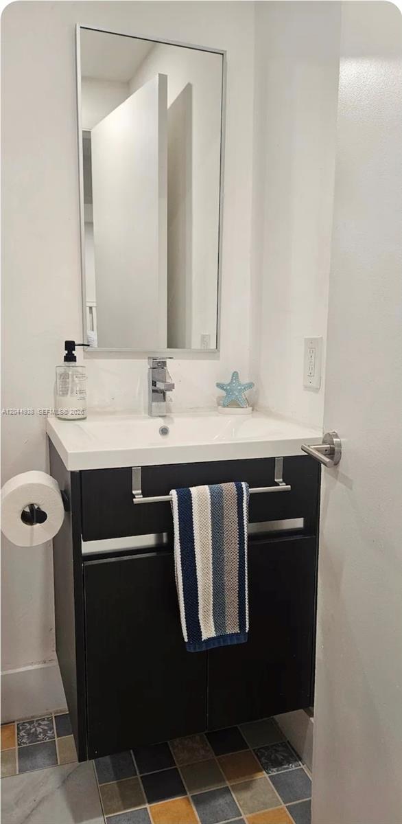 A small bathroom features a dark vanity, a white sink, a mirror, and tiled flooring — 144 NW 7th Ave # 2, Dania Beach FL 33004, DANIA BEACH, FL