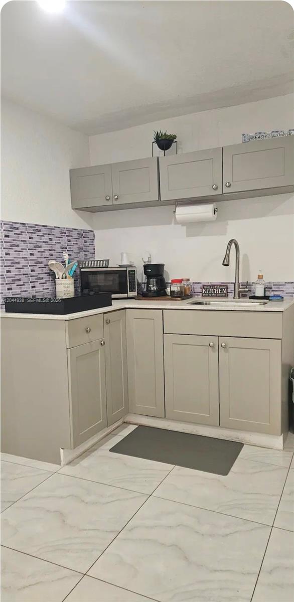 A small kitchen features light gray cabinets, a tiled backsplash, and a stainless steel sink — 144 NW 7th Ave # 2, Dania Beach FL 33004, DANIA BEACH, FL