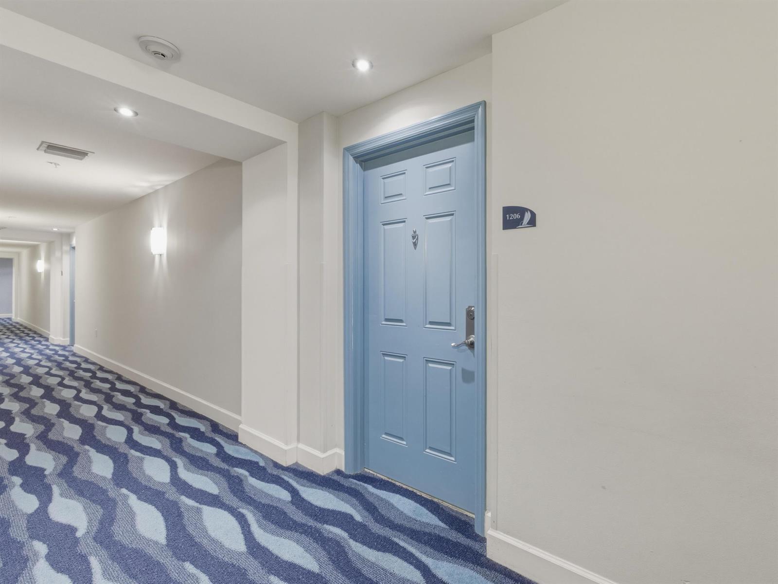 A blue door labeled 1206 sits in a hallway with patterned blue carpet — 625 Casa Loma Boulevard # 1206, Boynton Beach FL 33435, BOYNTON BEACH, FL