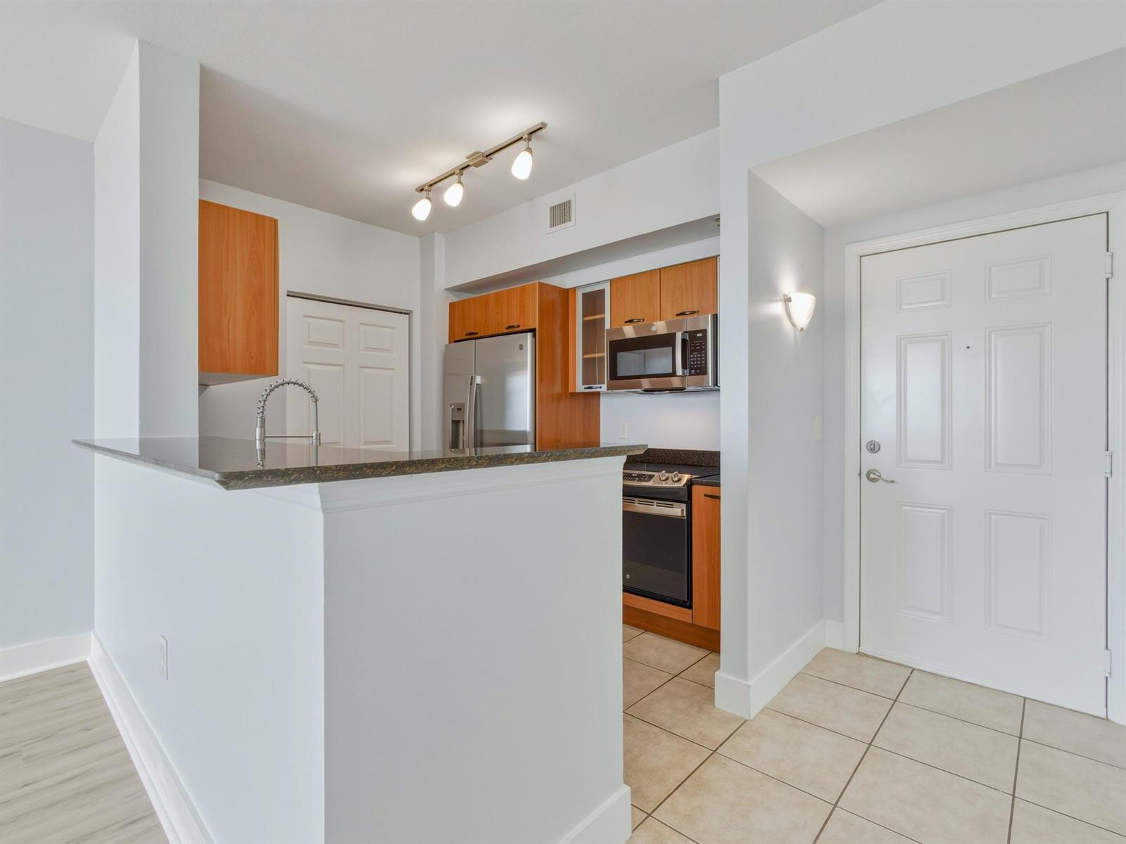 A kitchen with wood cabinets, stainless steel appliances, and a breakfast bar near an entryway — 625 Casa Loma Boulevard # 1206, Boynton Beach FL 33435, BOYNTON BEACH, FL