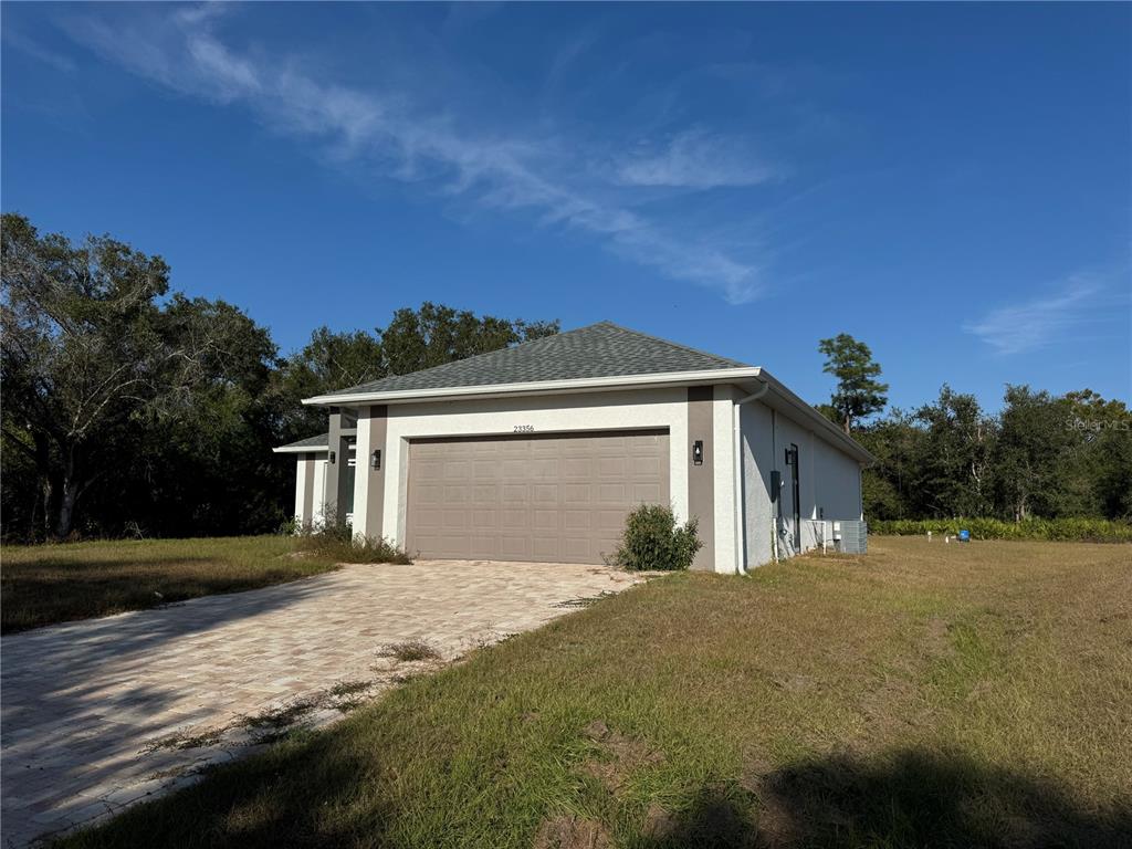 A single-story house with a two-car garage and a paved driveway under a blue sky — 23356 ROSEWOOD AVENUE, PUNTA GORDA, FL