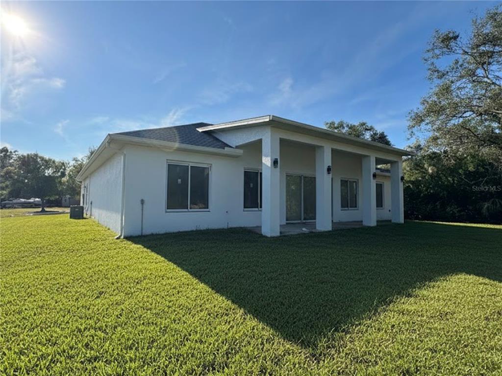 The exterior of a white stucco house features a covered patio and a large lawn — 23356 ROSEWOOD AVENUE, PUNTA GORDA, FL