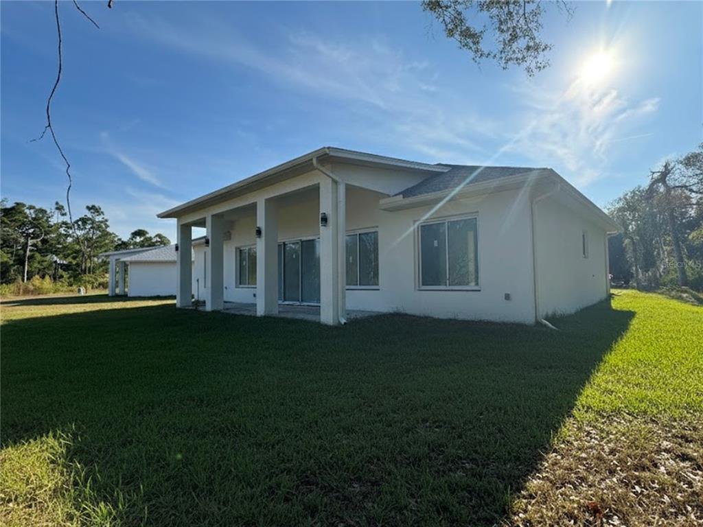 The exterior of a white house features a covered patio and a large grassy yard — 23356 ROSEWOOD AVENUE, PUNTA GORDA, FL