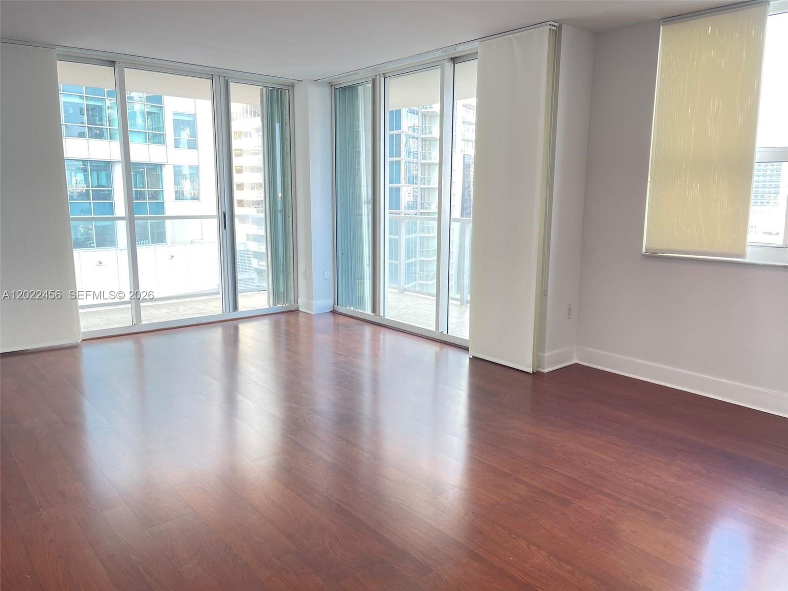 An empty room features hardwood floors, floor-to-ceiling windows, and a view of city buildings — 1155 Brickell Bay Dr # 1102, Miami FL 33131, MIAMI, FL