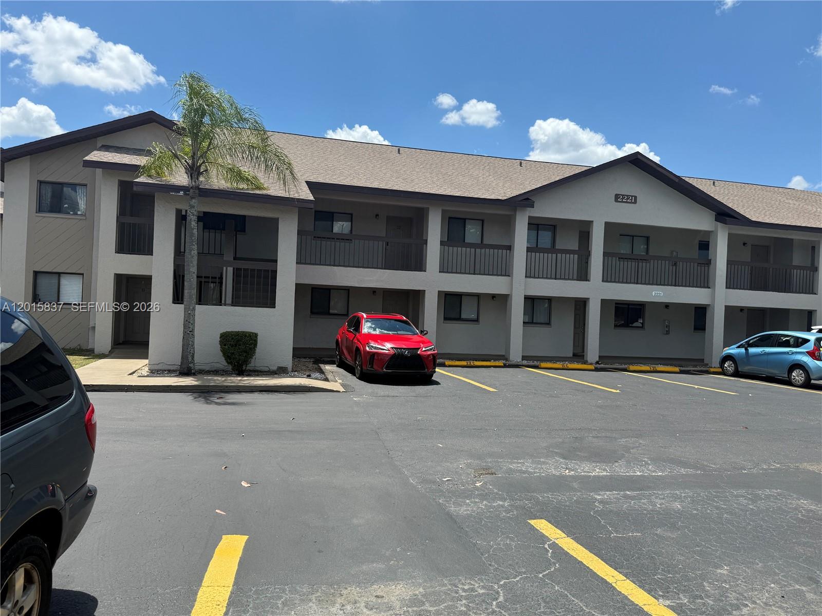 A two-story apartment building with a parking lot and a red car in front — 2221 E 5th street # 21, Lehigh Acres FL 33936, LEHIGH ACRES, FL