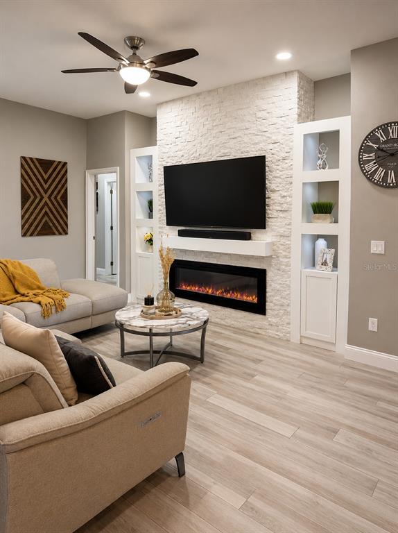 A living room features a stone fireplace wall with built-in shelving, a television, and light flooring — 9880 TIVOLI CHASE DRIVE, ORLANDO, FL