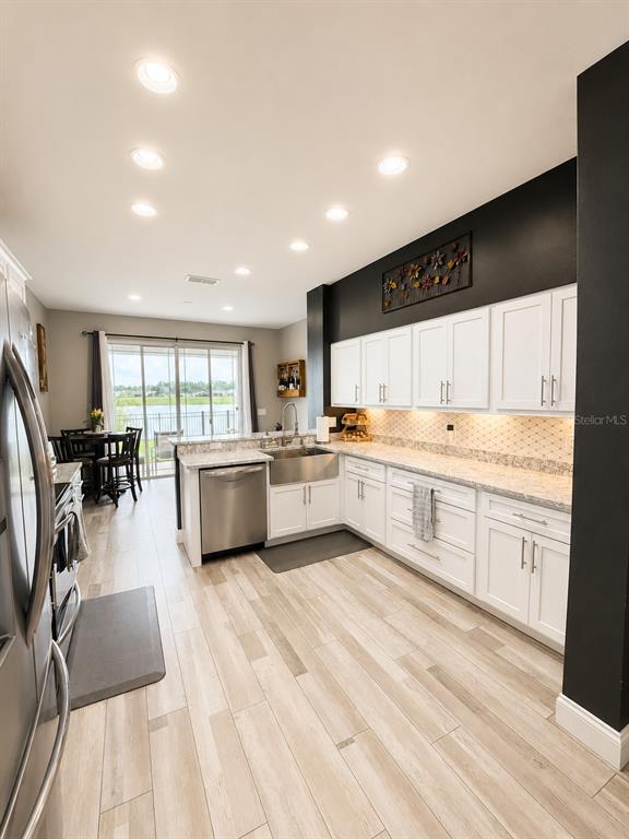 A kitchen features white cabinets, stainless steel appliances, light wood-look flooring, and a dark accent wall — 9880 TIVOLI CHASE DRIVE, ORLANDO, FL