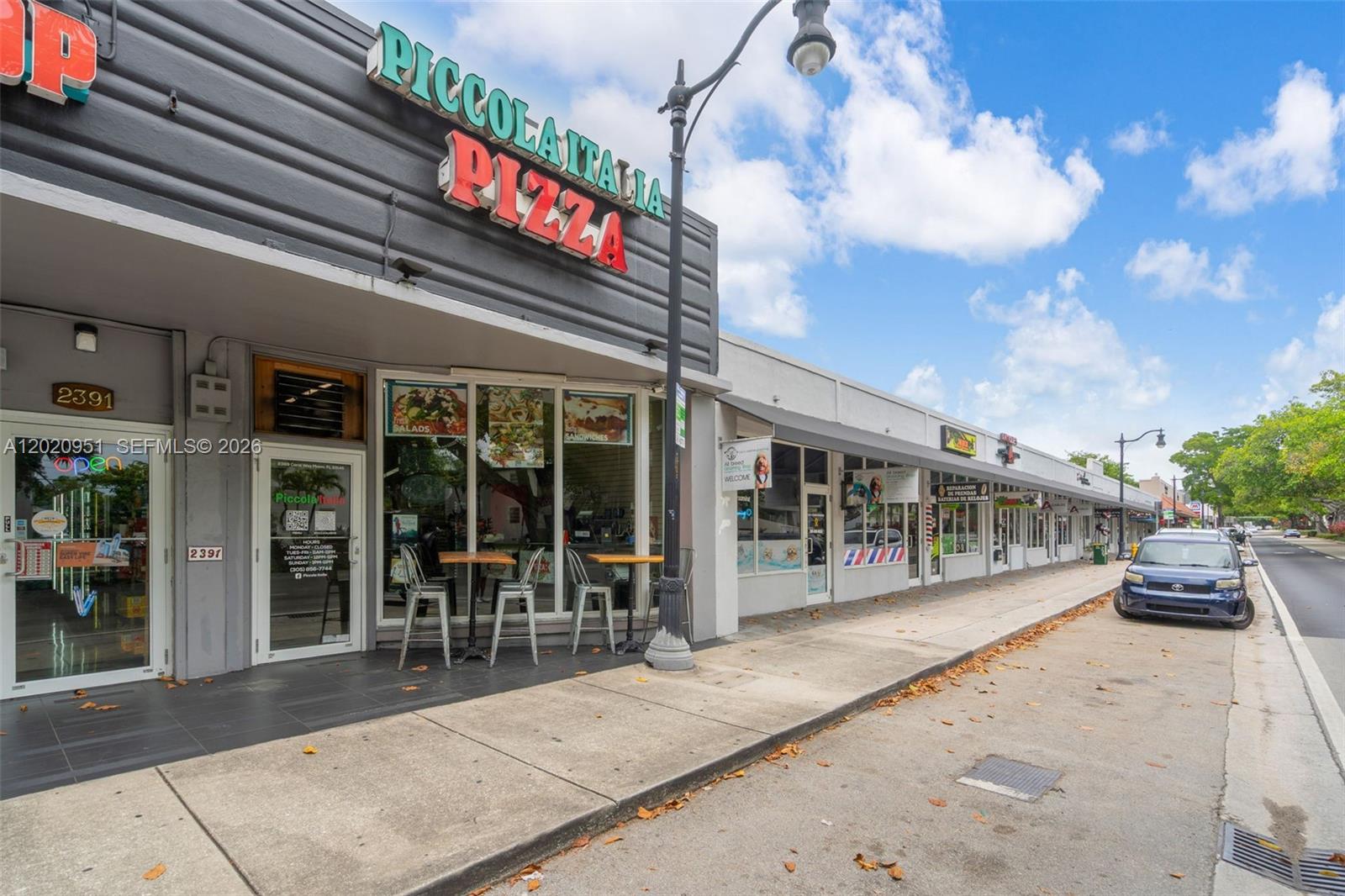 A row of commercial storefronts lines a sidewalk next to a street with a parked car — 2389 SW 22nd St, Miami FL 33145, MIAMI, FL