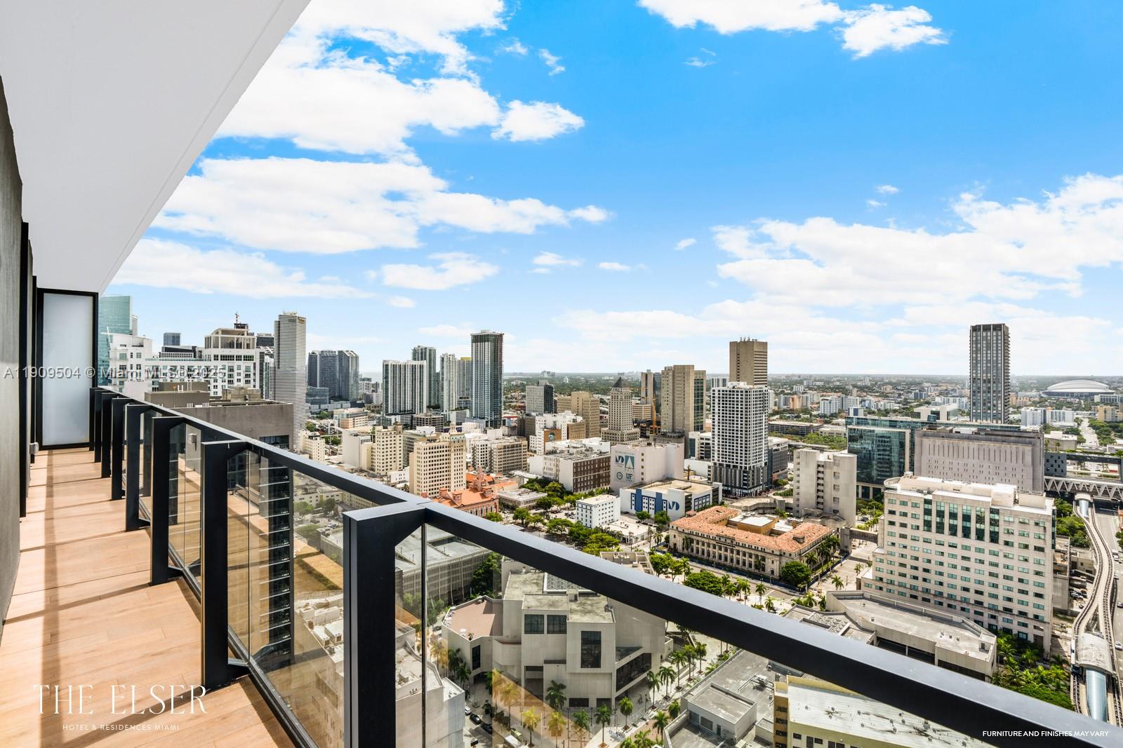A high-rise balcony with wood flooring and a glass railing overlooks a dense city skyline — 398 NE 5th St # 1601, Miami FL 33132, MIAMI, FL