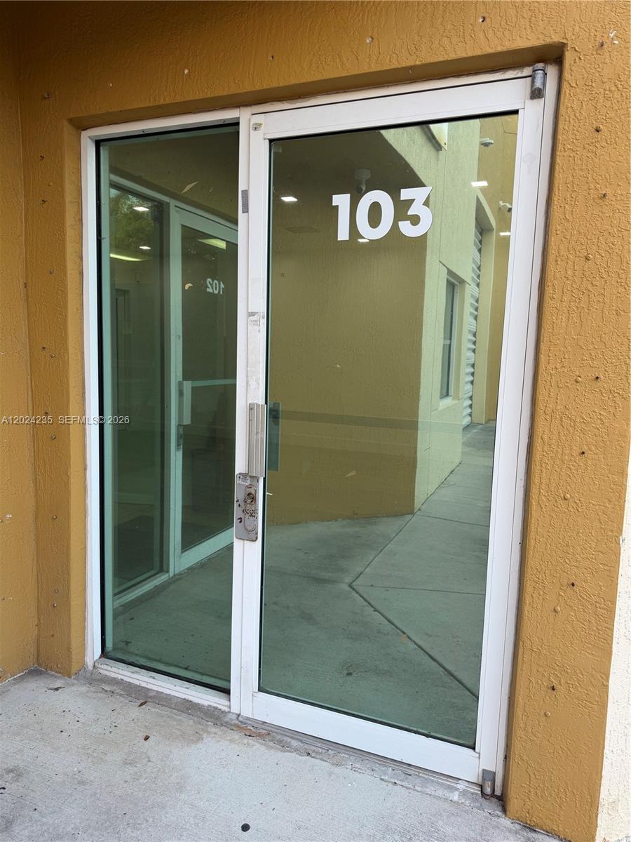 A glass-paned double door marked with the number 103 is set into a yellow stucco wall — 9450 NW 58th St # 3, Doral FL 33178, DORAL, FL
