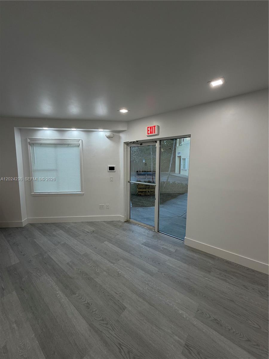 A room with grey wood-look flooring, a window with blinds, and a glass exit door — 9450 NW 58th St # 3, Doral FL 33178, DORAL, FL