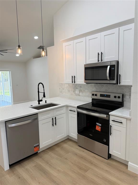 A kitchen features white cabinets, stainless steel appliances, a sink, and light wood flooring — 245 CHARDONNAY PLACE, VALRICO, FL
