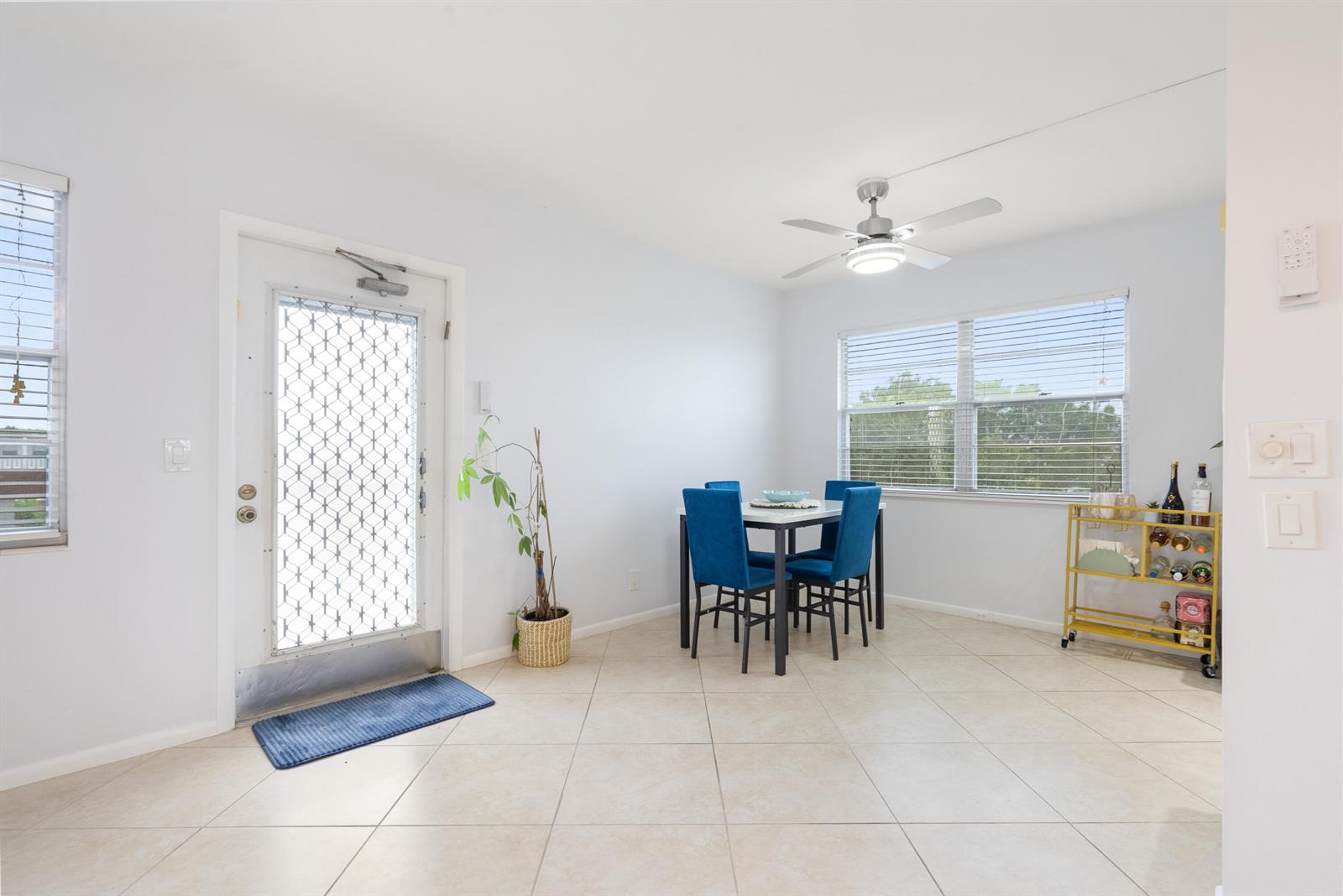 A dining area features tile floors, a ceiling fan, a table with blue chairs, and a door — 4060 Cornwall C, Boca Raton FL 33434, BOCA RATON, FL
